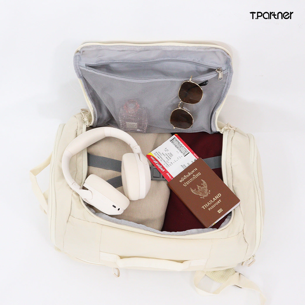 กระเป๋าเป้ Duffle สีครีมเปิดอยู่ แสดงให้เห็นของใช้เดินทาง เช่น หูฟัง หนังสือเดินทาง และแว่นกันแดด