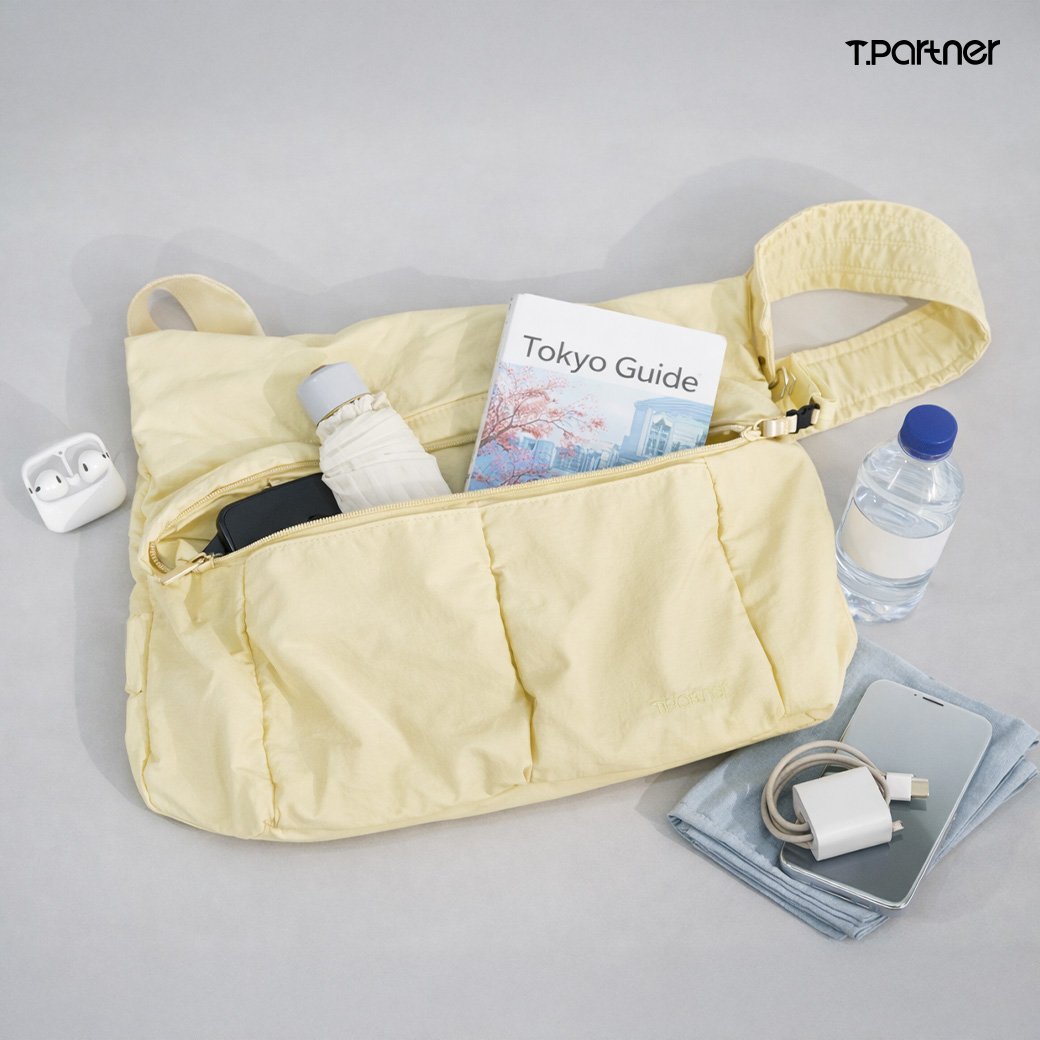 กระเป๋าสะพายข้างสีเหลืองอ่อน All Day Tote Bag วางโชว์ของใช้จำเป็น เช่น โทรศัพท์มือถือ สมุดคู่มือท่องเที่ยว และขวดน้ำ